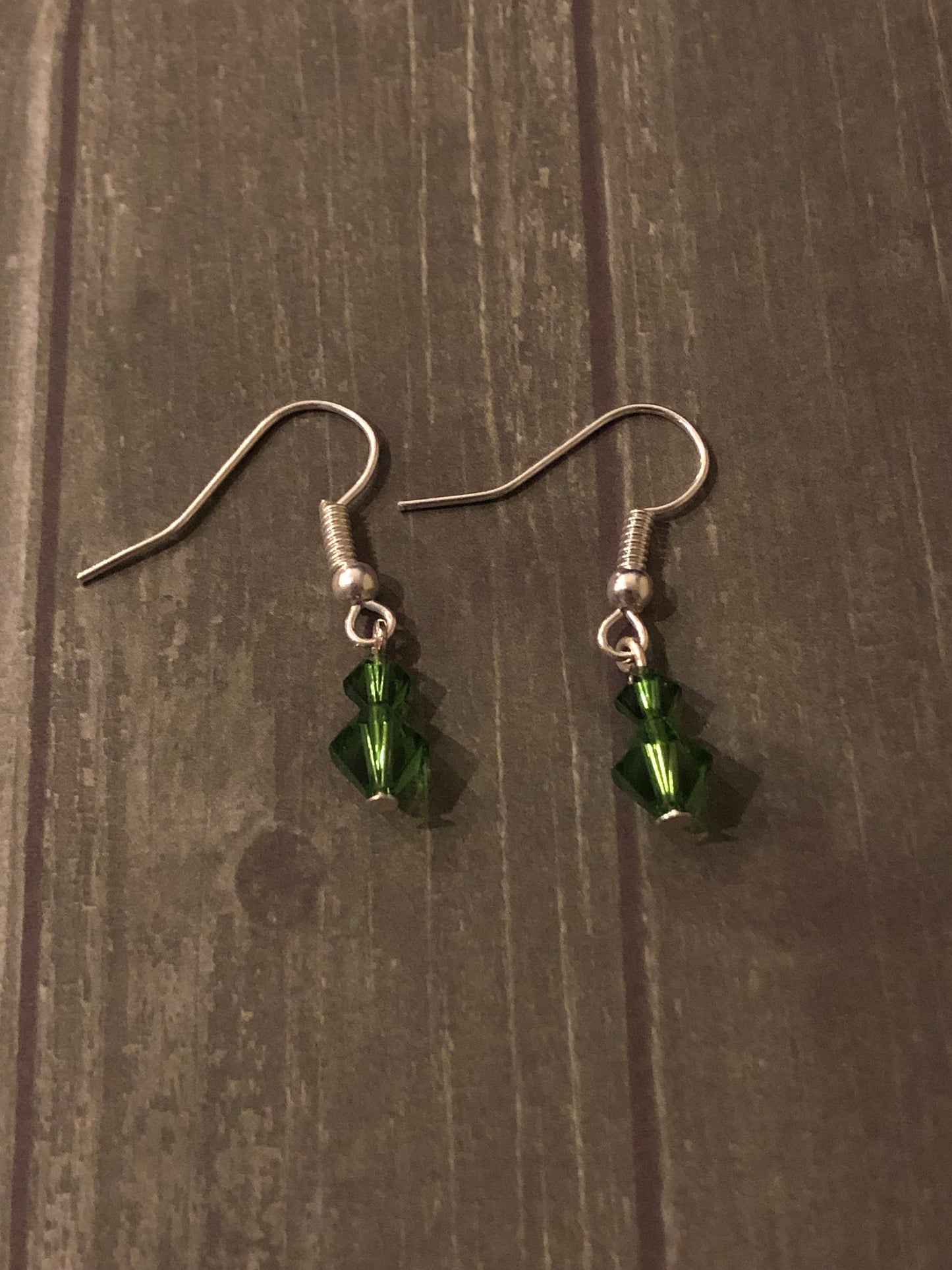 Silver earrings with 2 green crystal beads incorporated into the styling.